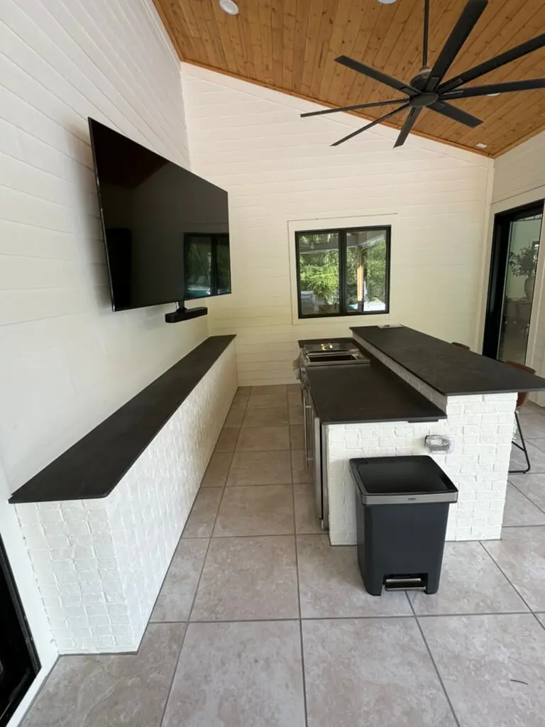 Outdoor patio with a wall-mounted TV, black countertop bar, ceiling fan, and tile flooring.