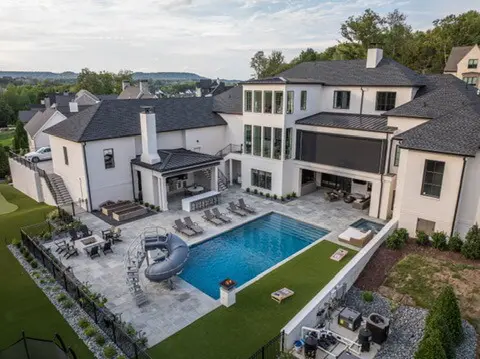 Aerial view of a large modern house with a pool, slide, and patio in a landscaped backyard.