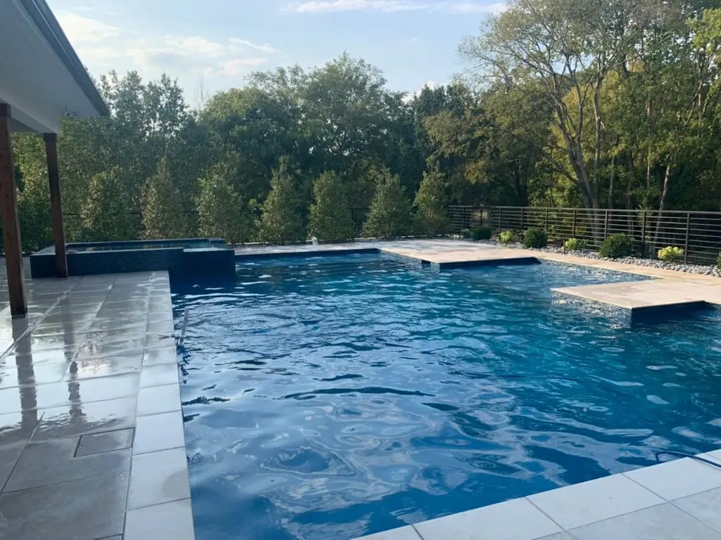 A large outdoor swimming pool with clear blue water, surrounded by trees and a tiled deck.