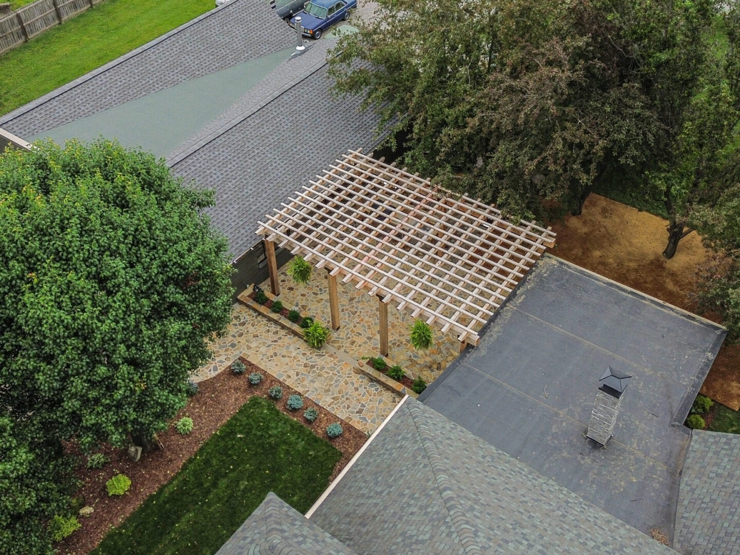 A wooden pergola structure in a backyard between two houses.