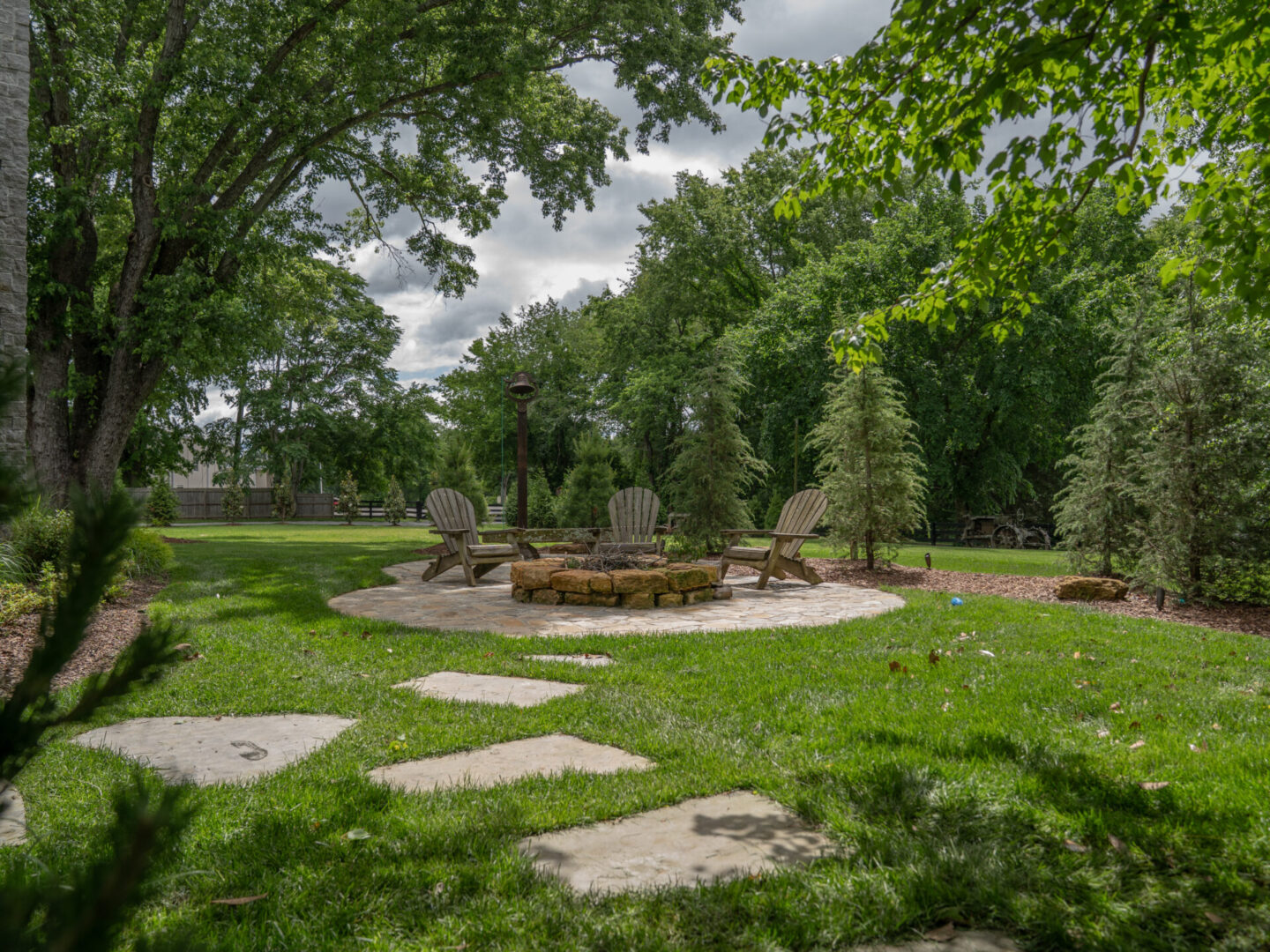 Serene garden with a stone path leading to a circular fire pit area surrounded by trees.