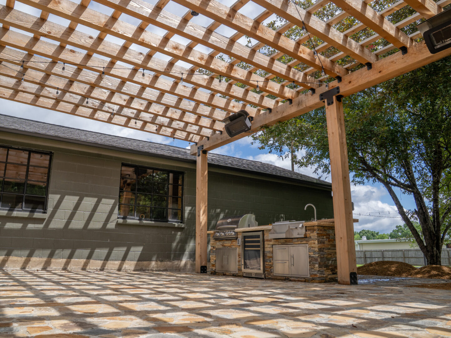 Outdoor patio with wooden pergola casting shadows and built-in grill area.