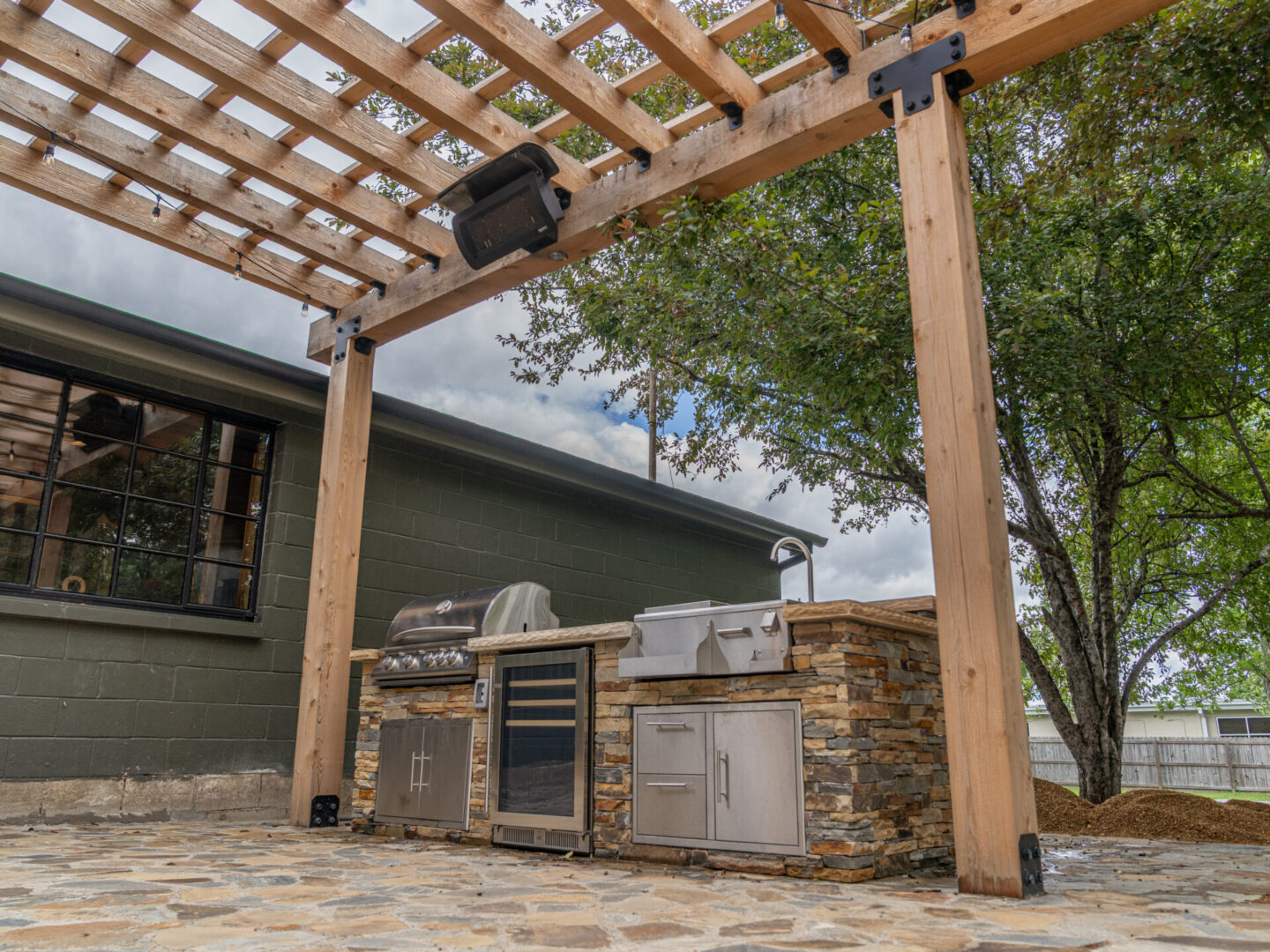 Outdoor kitchen setup with grill and stone countertops under a wooden pergola.
