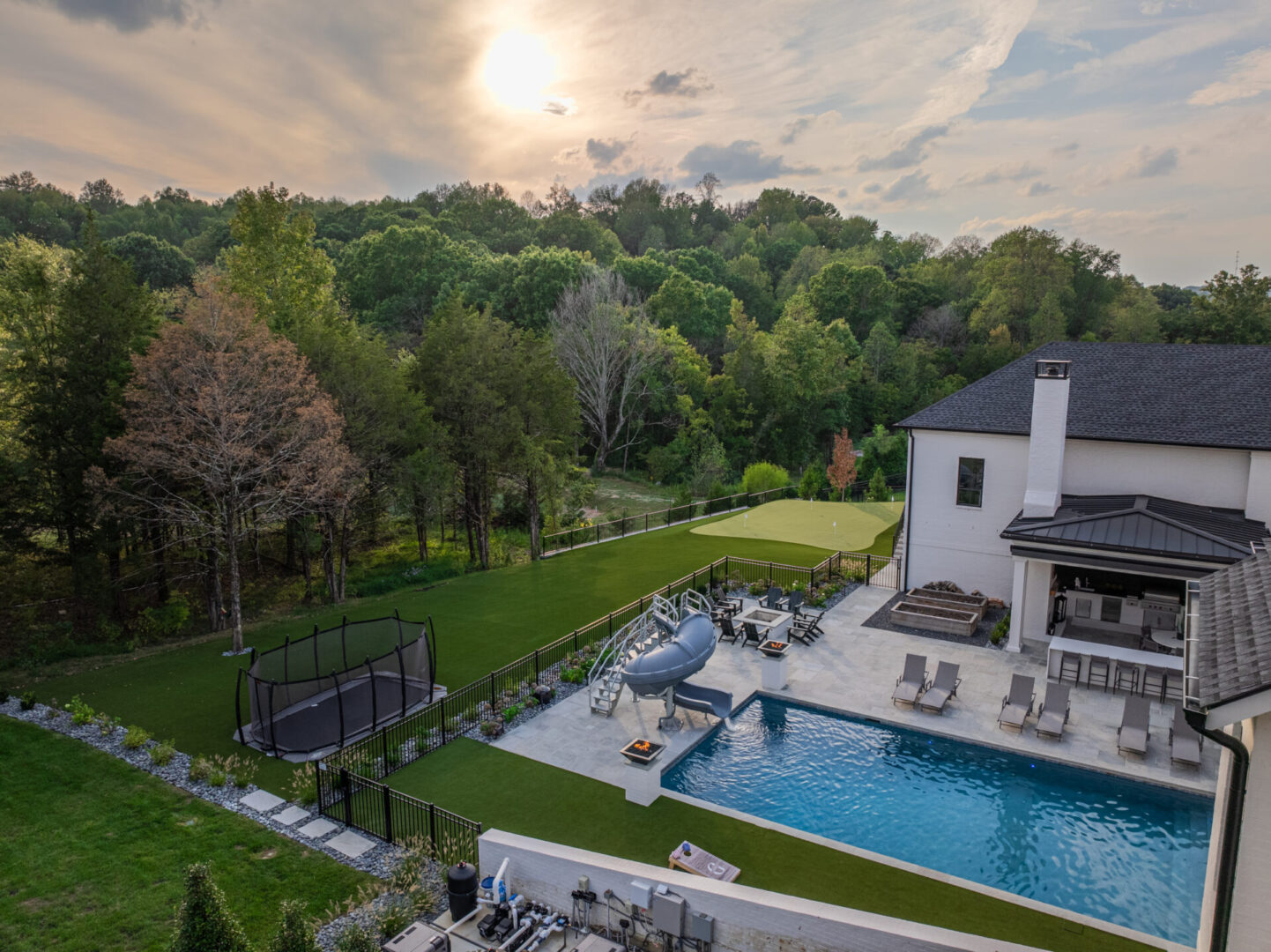 A serene backyard with a pool and lush greenery at sunset.